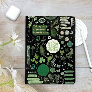 May include: A black journal with green botanical and inspirational graphics. Text includes "Taking care of yourself is productive" and "It is all a part of the process". The journal also has butterflies, clovers, and the words "I am beautiful".