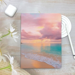 Könnte beinhalten: Ein rosa und orangefarbener Sonnenuntergang über einem türkisfarbenen Meer mit weißen Wellen, die an einem Sandstrand brechen.