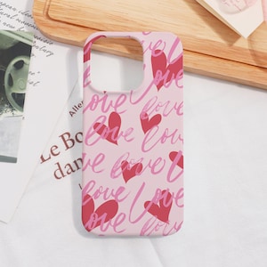May include: A pink phone case with a repeating pattern of red hearts and the word "love" in a cursive font. The case has cutouts for the camera and buttons.