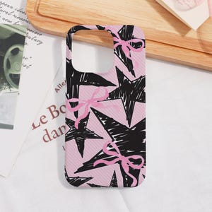 May include: A smartphone case featuring a pink background with a pattern of black stars and pink bows. The case is designed to fit a mobile phone and has cutouts for the camera and buttons.