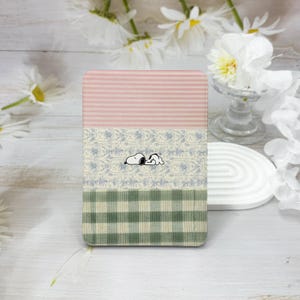 May include: A rectangular case featuring Snoopy. The top section has pink and white stripes, the middle section has a floral pattern, and the bottom section has a green and white plaid pattern.