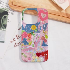 May include: A vibrant phone case with a patchwork design. It features a butterfly, hearts, flowers, and the word "LOVE". The background includes denim, gingham, and floral patterns, with pink, blue, and red hues.