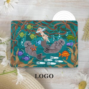 May include: A rectangular laptop skin featuring a teal underwater scene with two brown sea otters, a jellyfish, various colorful fish, and brown kelp. One otter holds an orange starfish, and the design incorporates a central Apple logo cutout.