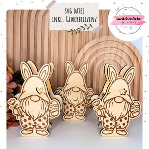 Op de afbeelding: Houten Paas kabouter beeldjes met konijnenoren, met een ei en een bloem. De kabouters dragen outfits met stippen. De afbeelding bevat de tekst "SVG DATEI INKL. GEWERBELIZENZ" en een logo "Laedchenliebe DESIGNS".