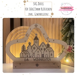 Könnte beinhalten: Eine hölzerne Weihnachtsdorf-Szene mit Kirche, Häusern und Bäumen, ausgeschnitten in Sternform. Die Basis trägt die Worte "frohe WEIHNACHTEN" und eine Schneeflocke. Der Text "SVG DATEI FÜR 160x22MM KLÖTZCHEN INKL. GEWERBELIZENZ" befindet sich oben.