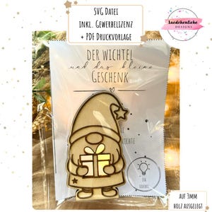 Pode incluir: Decoração de madeira em forma de gnomo segurando um presente, com o texto "DER WICHTEL und das kleine GESCHENK". A imagem inclui o texto "SVG DATEI INKL. GEWERBELIZENZ + PDF DRUCKVORLAGE" e "AUF 3MM HOLZ AUSGELEGT".