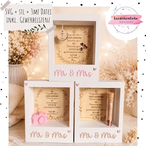 Könnte beinhalten: Drei weiße quadratische Schattenboxen mit dem Schriftzug Mr & Mrs in Rosa oder Beige. Jede Box enthält eine Holzplatte mit deutschem Text und floralen Gravuren. Eine Box enthält eine kleine rosa Kamera, eine andere ein Glasröhrchen und eine ein Anhängeschild.