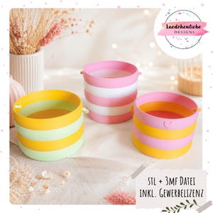 May include: Three colorful, collapsible containers. One is yellow and green striped, another is pink and white striped, and the third is pink and yellow striped. The containers have small handles and are on a white surface.