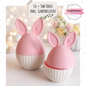 May include: Two pink and white Easter egg-shaped containers with bunny ears. The containers have a ribbed white base and a pink top with heart-shaped details on the ears. The text "STL + 3MF DATEI INKL. GEWERBELIZENZ" is visible.