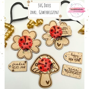 May include: Wooden laser-cut decorations featuring ladybugs on clovers and a mushroom, with small tags that say "Happy 2026", "Happy New Year", and "eine Kleinigkeit". The image also includes the text "SVG DATEI INKL. GEWERBELIZENZ".