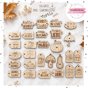 Op de afbeelding: Een verzameling lichtgekleurde houten labels met lasergegraveerde herfstmotieven zoals pompoenen, paddenstoelen, paraplu's, sokken en eikels, samen met teksten zoals "hallo HERBST", "cozy AUTUMN" en "fall IN LOVE".