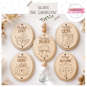 May include: Five circular wooden ornaments with laser-engraved autumn designs including acorns, a mushroom, socks, a pumpkin, and an umbrella. The centre ornament features a hanging string with wooden beads and a clear faceted crystal pendant.