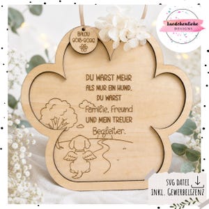 Può includere: Una targa in legno chiaro a forma di zampa con un'illustrazione incisa di un cane con le ali su un sentiero, un albero e il testo in tedesco: DU WARST MEHR ALS NUR EIN HUND. DU WARST FAMILIE, FREUND UND MEIN TREUER BEGLEITER. Include una piccola etichetta circolare.
