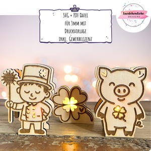Może przedstawiać: Wycinanki z drewna przedstawiające kominiarza, czterolistną koniczynę i świnię, każda z nich ma w środku światło. Kominiarz trzyma miotłę i nosi cylinder. Świnia ma czterolistną koniczynę na piersi. Tekst na znaku brzmi "SVG + PDF DATEI FÜR 3MM MIT DRUCKVORLAGE INKL. GEWERBELIZENZ."