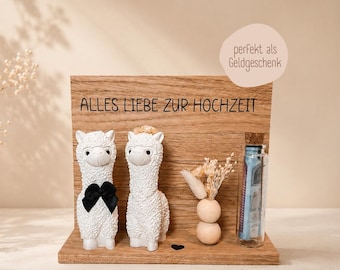 May include: A wooden wedding gift with two white alpaca figurines, one with a black bow tie. The wooden plaque has the text "ALLES LIEBE ZUR HOCHZEIT". A small glass bottle with money and a small wooden vase with dried flowers are also included.