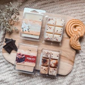 Könnte beinhalten: Draufsicht auf Wachsschmelzen in transparenten Kunststoffbehältern, eine Schokoladentafel und ein Keks auf einem Holzbrett. Die Wachsschmelzen sind mit "Brownie Bites" und "Creme Vanille" beschriftet. Die Wachsschmelzen sind beige und braun.