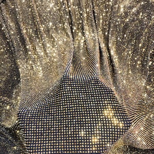 May include: A close-up of a gold fabric with a sparkly, diamond-like texture. The fabric is made of a mesh material with small, round sequins.