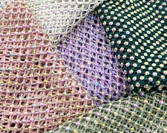 May include: Close-up of five different colors of mesh fabric with rhinestones. The colors are white, light purple, pink, green, and a darker green. The fabric is made of a fine mesh with small rhinestones.