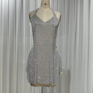 Puede incluir: Un vestido plateado corto de estilo halter hecho completamente de pedrería. El vestido tiene un corpiño ajustado y una falda acampanada.