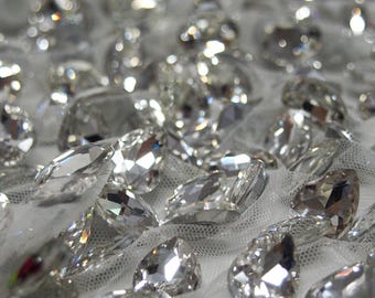 May include: Close-up of a white mesh fabric covered in clear, faceted rhinestones. The rhinestones are arranged in a random pattern and create a sparkling effect.