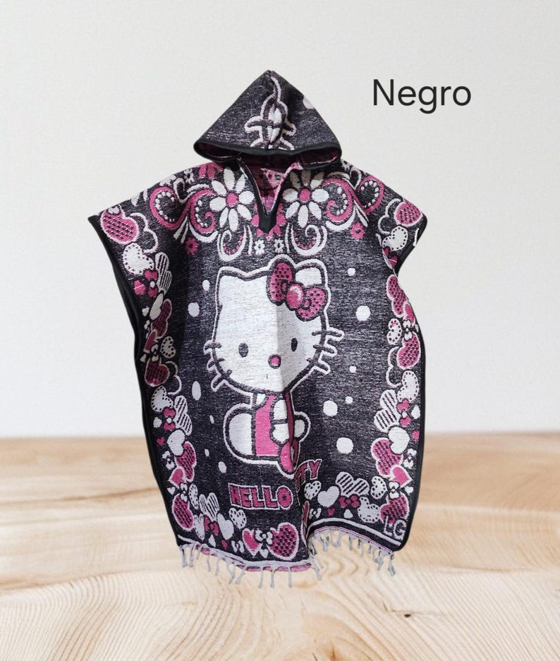 May include: Black hooded poncho with a Hello Kitty design in white and pink. The poncho is decorated with pink and white floral and heart patterns. The word "Hello" is visible on the front. The word "Negro" is written on the top right.