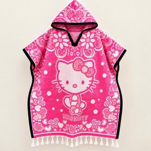 May include: A bright pink hooded poncho towel featuring a white Hello Kitty graphic, a bow, and the text Hello Kitty. The design includes floral and heart patterns with white polka dots, finished with a black trim and white fringe at the bottom.