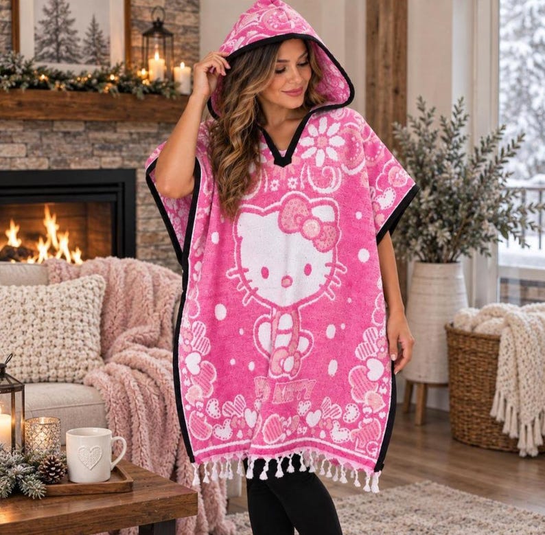 May include: A bright pink hooded poncho towel featuring a large white Hello Kitty graphic, a repeating floral and heart pattern, and black trim along the edges. The garment has a V-neckline and a hem finished with white fringe tassels.