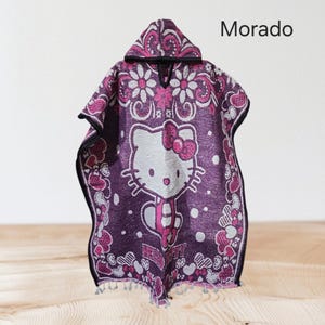 May include: Purple hooded poncho with a Hello Kitty design in white and a pink bow. The poncho has a floral and heart pattern with the word "Morado" printed on the top right.