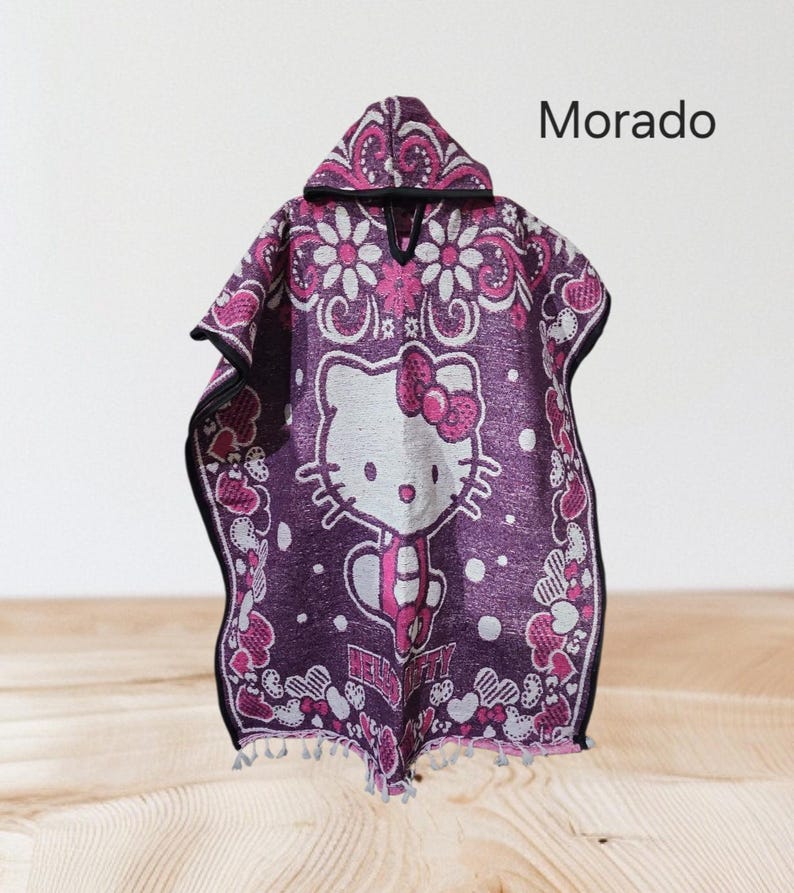 May include: Purple hooded poncho with a Hello Kitty design in white and a pink bow. The poncho has a floral and heart pattern with the word "Morado" printed on the top right.