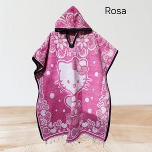 May include: Pink hooded poncho with a Hello Kitty design. The poncho has a white floral pattern and a black trim. The word "Rosa" is printed on the top right corner.