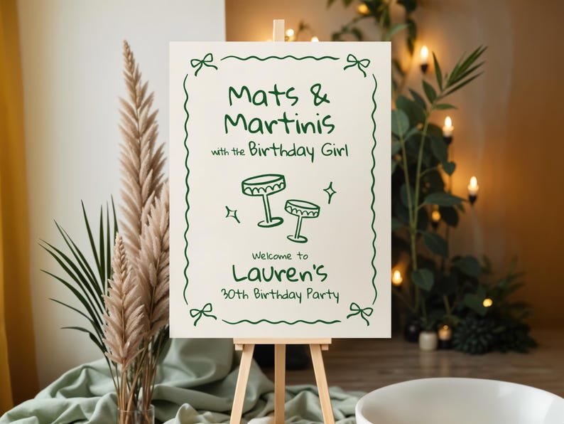 Pu&ograve; includere: Un cartello color crema su un cavalletto di legno con testo e illustrazioni verdi. Il cartello recita "Mats & Martinis with the Birthday Girl" e d&agrave; il benvenuto a "Lauren's 30th Birthday Party."