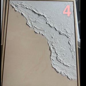 Op de afbeelding: Abstract kunstwerk met een getextureerd wit golfontwerp op een lichtbeige achtergrond, omlijst in natuurlijk hout. Het nummer "4" is roze zichtbaar. Kustthema.