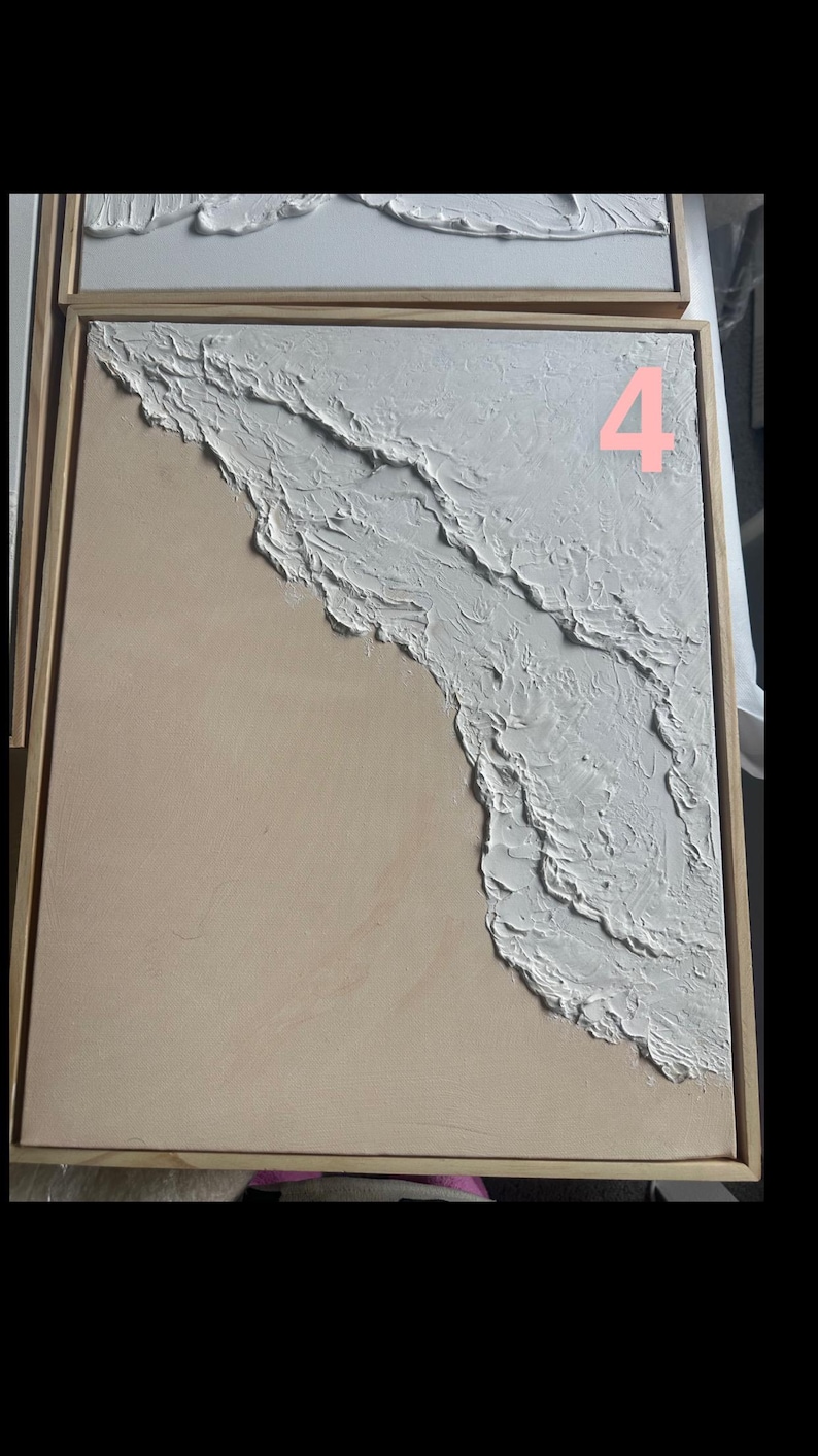 Op de afbeelding: Abstract kunstwerk met een getextureerd wit golfontwerp op een lichtbeige achtergrond, omlijst in natuurlijk hout. Het nummer "4" is roze zichtbaar. Kustthema.