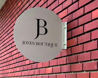 May include: A white round sign with black text that reads "JONES BOUTIQUE" and a black letter "B" in a stylized font.
