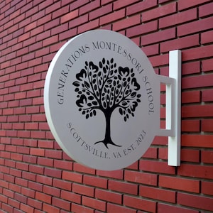 May include: A white round sign with black text and a tree design. The text reads "Generations Montessori School Scottsville, VA Est. 2023".