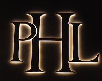 Può includere: Un cartello nero illuminato con le lettere "PHL" in un carattere grassetto sans-serif.