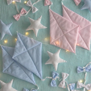 May include: A blue and pink fabric mobile with stars and bows. The mobile is made of soft fabric and is perfect for a baby's nursery.