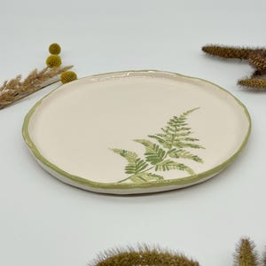 Puede incluir: Un plato pequeño, redondo, de cerámica blanca con un borde verde y un diseño de helecho verde.