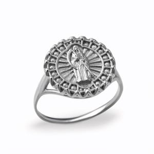 May include: A silver ring featuring a detailed central design of a robed figure with a scythe, surrounded by a sunburst pattern within a decorative, circular frame. The ring has a polished finish and a simple band.