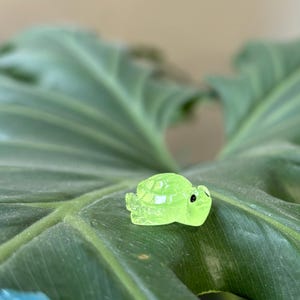 May include: A small, green glass turtle figurine with black eyes. The turtle is sitting on a green leaf.