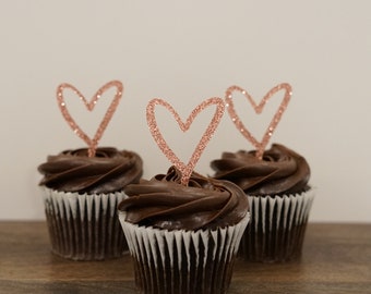 May include: Three chocolate cupcakes topped with rose gold glitter heart cupcake toppers.