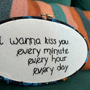 Może przedstawiać: Białe tamborek do haftu z haftowanym czarnym napisem "i wanna kiss you... every minute every hour every day" na białym tle. Tamborek ma niebiesko-czarną zewnętrzną krawędź z nadrukiem galaktyki.