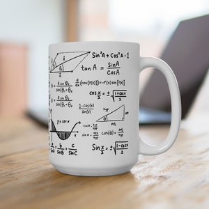 May include: White ceramic mug with black mathematical formulas and equations printed on the front. The mug has a large handle and is sitting on a wooden surface.