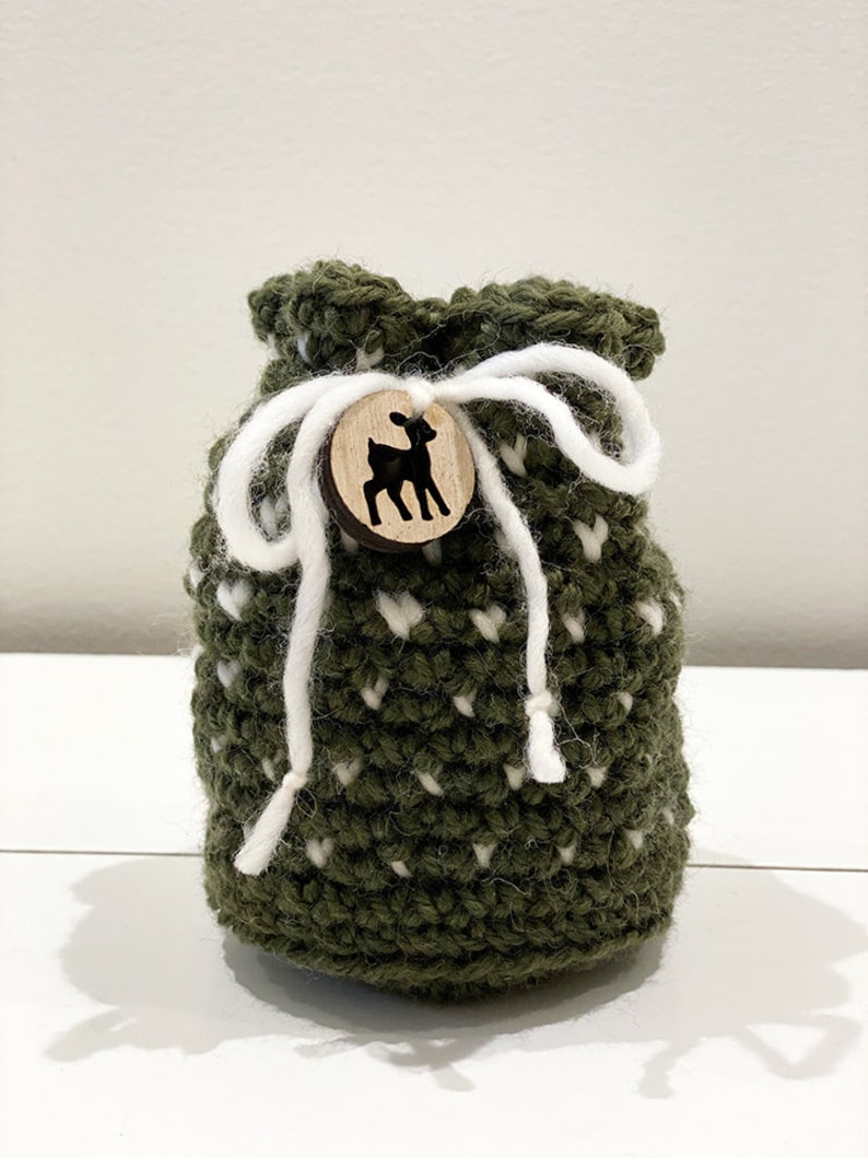 May include: A green crocheted drawstring bag with white polka dots and a wooden button featuring a deer silhouette.