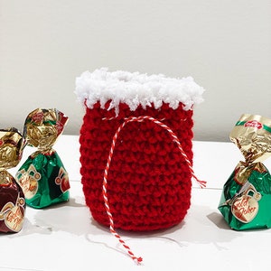 May include: A small red crocheted bag with a white crocheted trim and a red and white string tie. The bag is filled with wrapped chocolates.