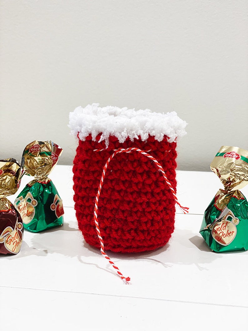 May include: A small red crocheted bag with a white crocheted trim and a red and white string tie. The bag is filled with wrapped chocolates.