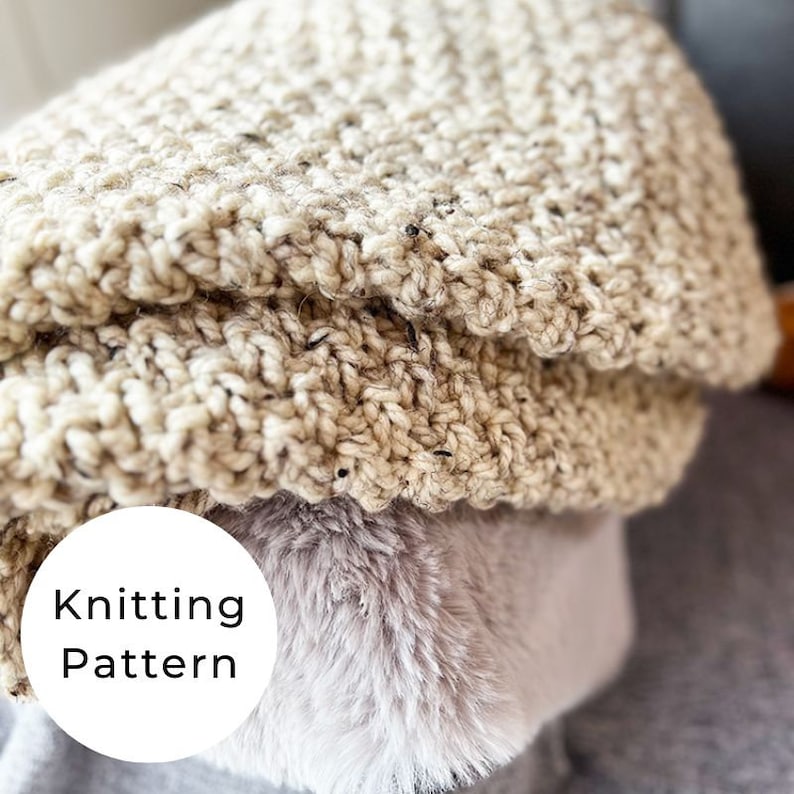May include: A close-up of a beige knitted blanket with a textured pattern. The blanket is folded over and the edges are visible. The text "Knitting Pattern" is written in a white circle on the bottom left corner of the image.