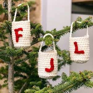 May include: Three white crocheted Christmas ornaments with red felt letters spelling "FJL" hanging on a green Christmas tree.