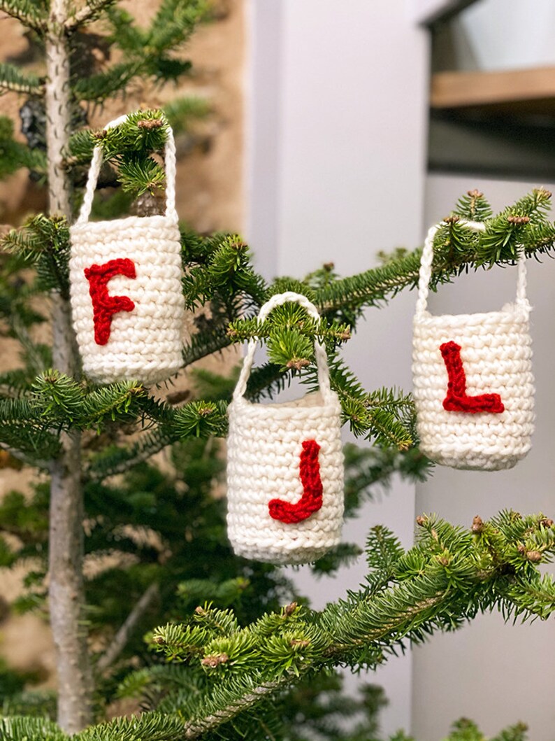 May include: Three white crocheted Christmas ornaments with red felt letters spelling "FJL" hanging on a green Christmas tree.