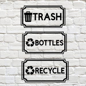 May include: Three black and white rectangular signs for waste management. The top sign reads "TRASH" with a trash can icon. The middle sign says "BOTTLES" with a recycling symbol. The bottom sign says "RECYCLE" with a recycling symbol.